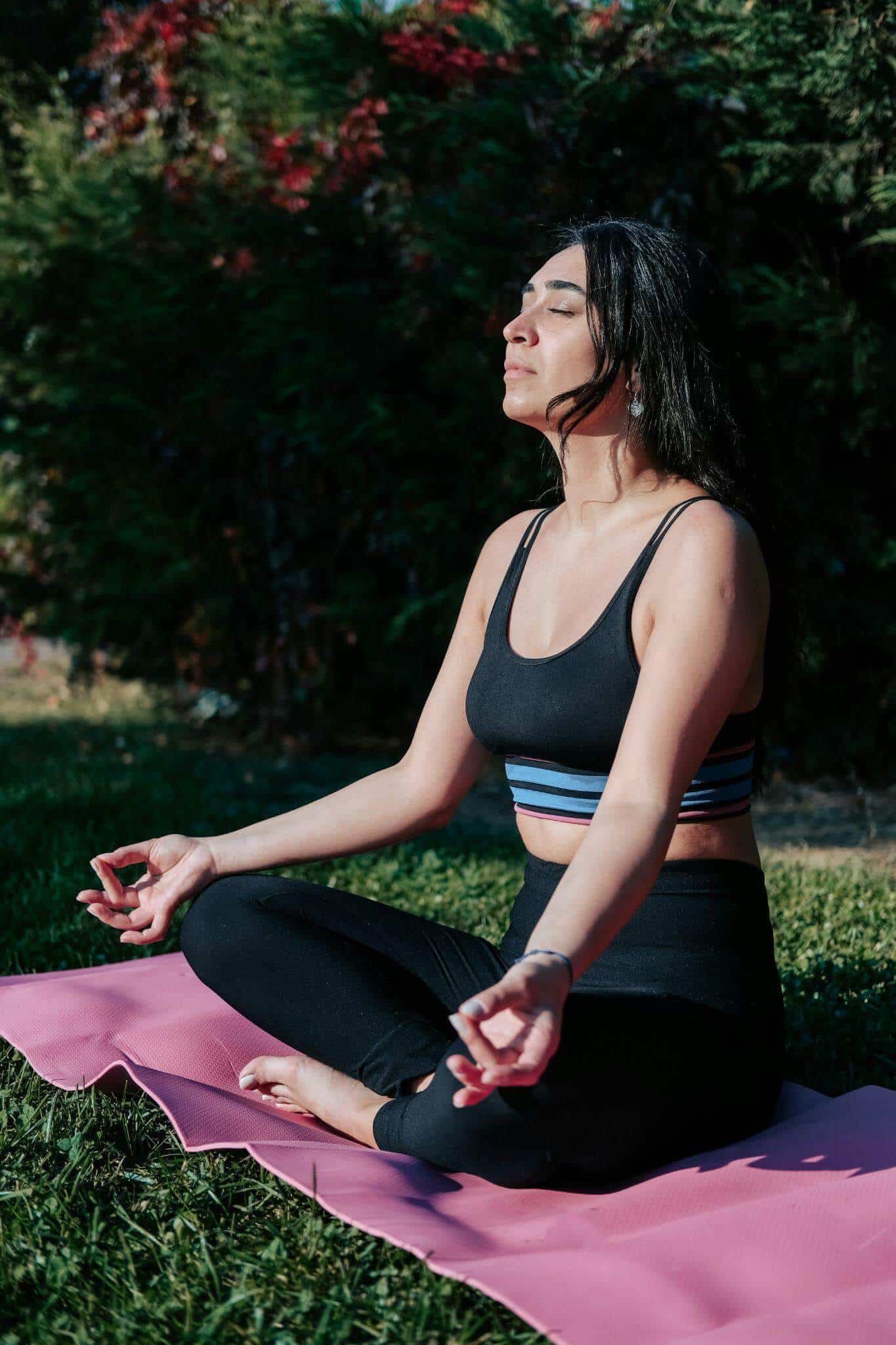 A woman taking a deep breath, not shallow breathing, on a yoga mat in the park